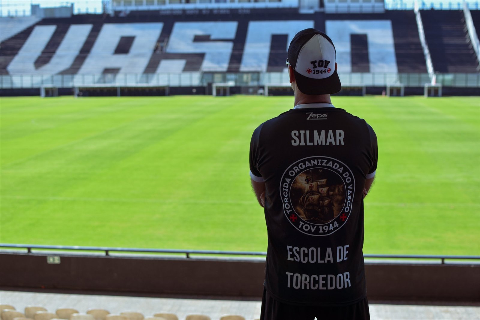 Integrante da TOV com a camisa Escola de Torcedor diante do gramado de São Januário